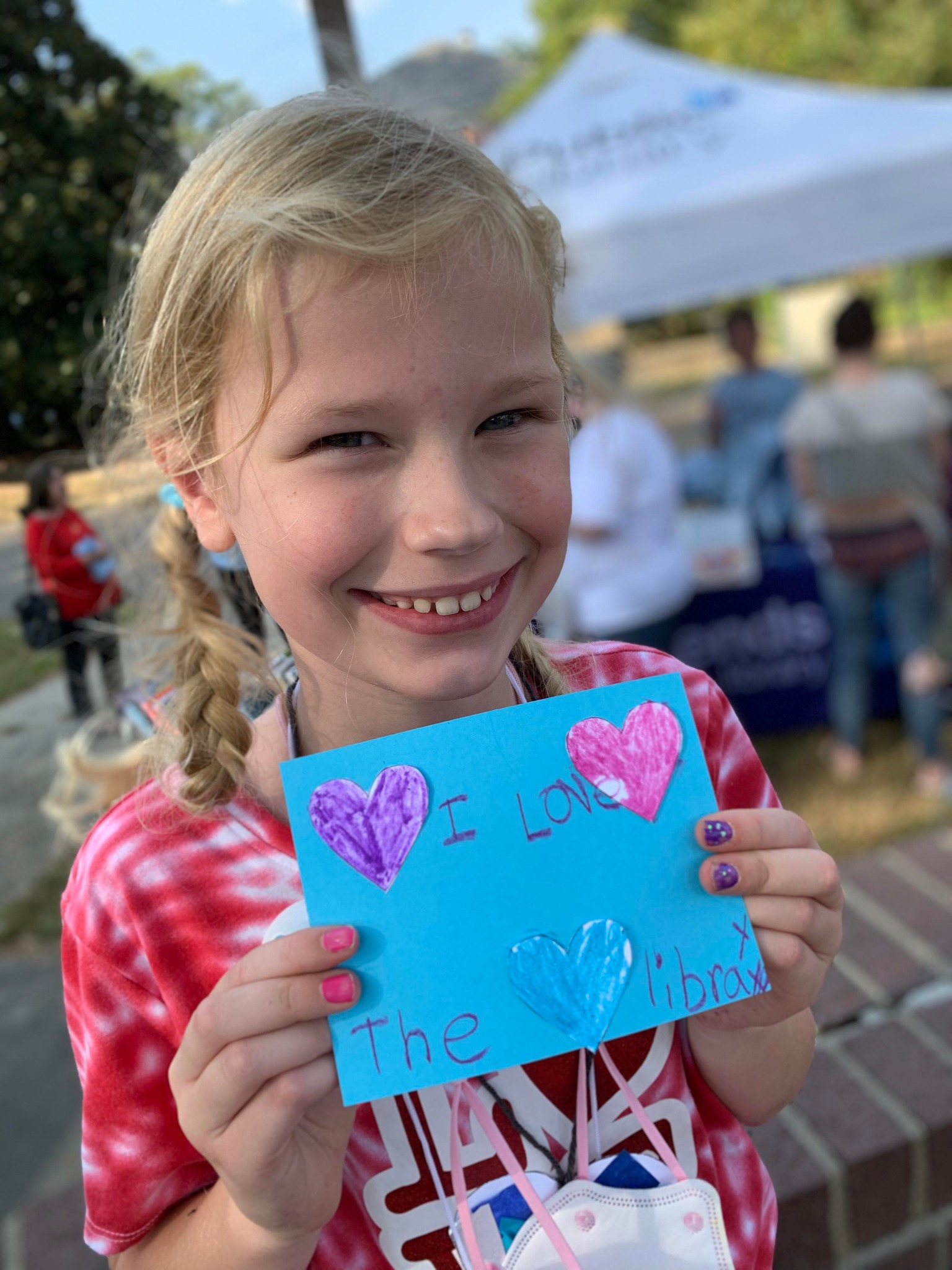 A young girl poses with a hand-made sign that reads "love the library"